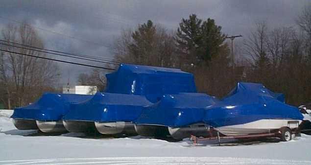 A collection of boats sitting outside in the snow with a blue tarp over them.
